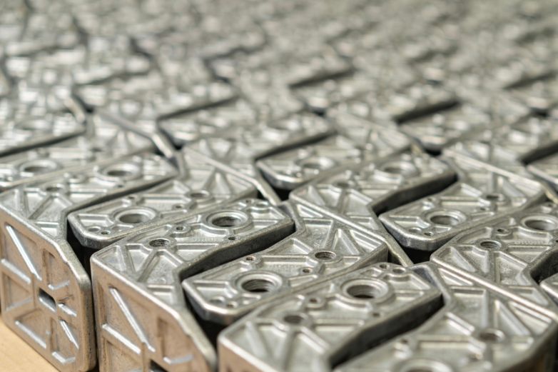 Rows of identical die-cast metal brackets with ribbed backs; a Dynacast group image, not tied to a specific plant