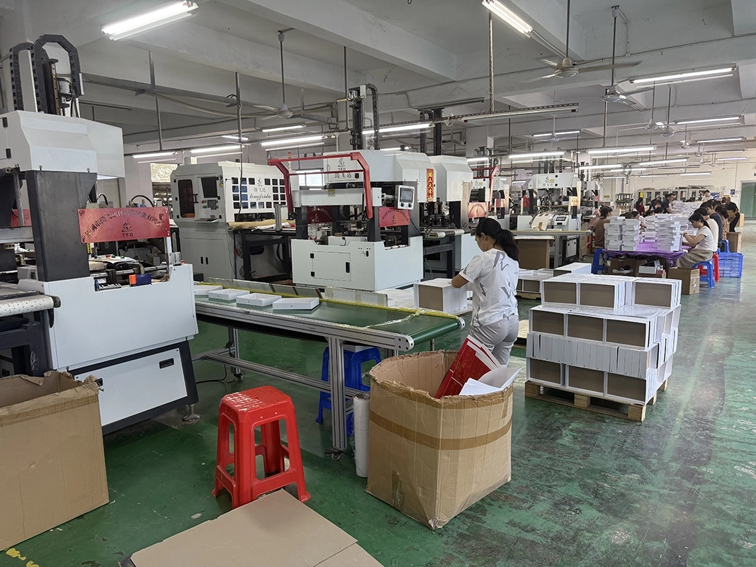 Rigid box assembly workshop with box-forming machines and stacks of finished white boxes