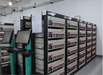 Racks of battery cyclers with monitoring screens on the production floor
