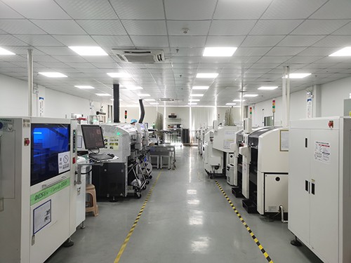 SMT workshop with a row of white placement machines and an inspection station