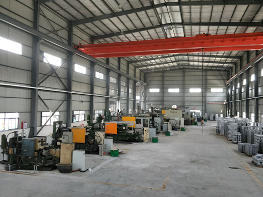 High-bay die casting hall with an orange overhead crane, a row of die casting machines on the left and stacked castings on the right