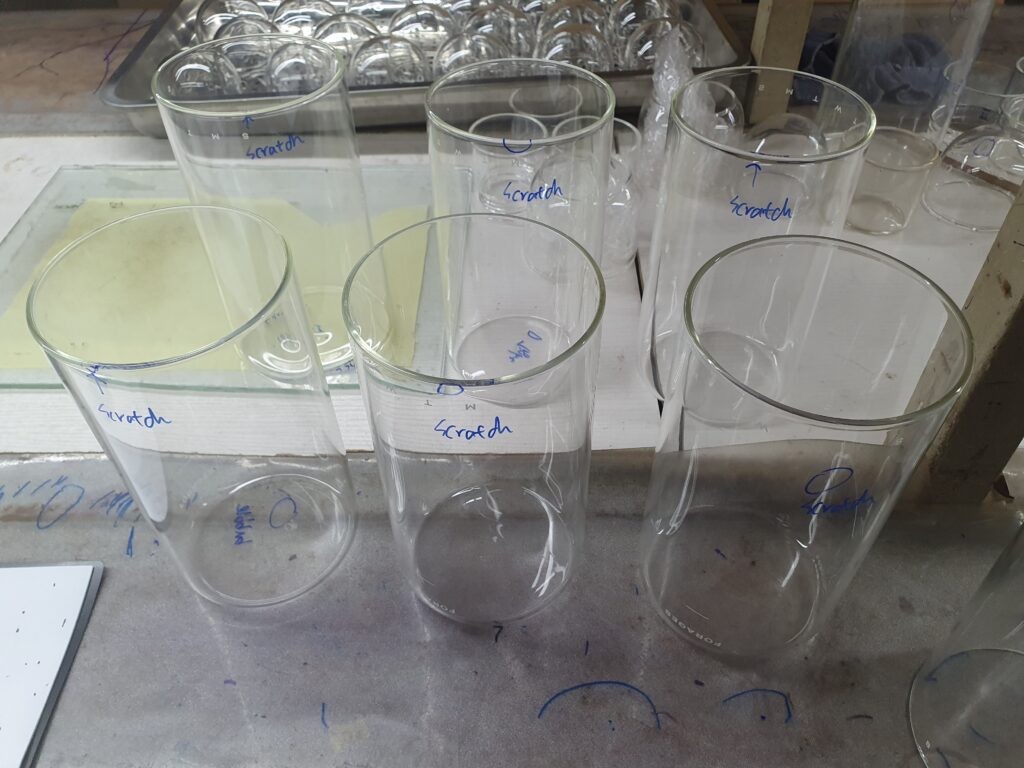 Clear glass jars on an inspection table, marked in blue pen where scratches were found